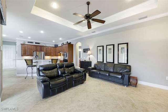 10026 Lions Bay Ct, Naples, FL 34120 - living room with a tray ceiling, ornamental molding, ceiling fan, arched walkways, and light tile patterned flooring