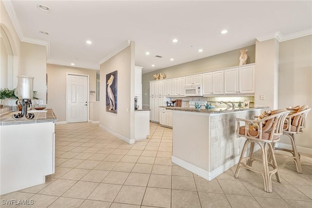 9121 Southmont Cv Unit 204, Fort Myers, FL 33908 - kitchen featuring white microwave, tasteful backsplash, a peninsula, crown molding, and white cabinets