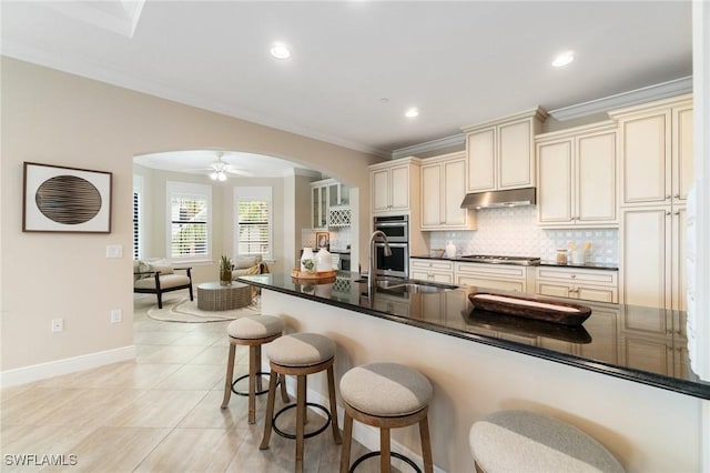 2768 Tiburon Blvd E Unit 202, Naples, FL 34109 - kitchen featuring cream cabinets, arched walkways, under cabinet range hood, dark countertops, and a sink