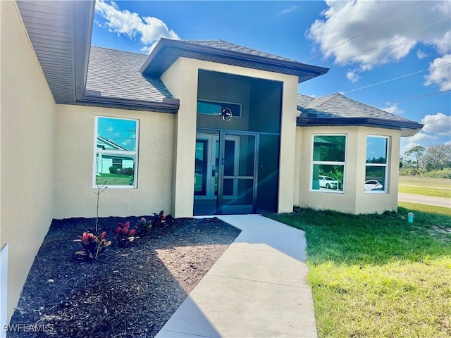 3319 17th St W, Lehigh Acres, FL 33971 - view of exterior entry with roof with shingles, stucco siding, and a yard
