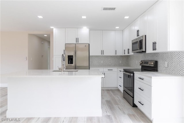 4779 31st Pl SW, Naples, FL 34116 - kitchen featuring appliances with stainless steel finishes, a sink, an island with sink, light wood-style floors, and white cabinets