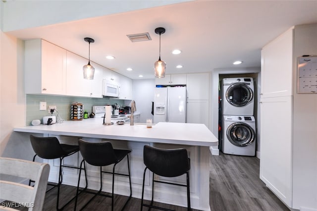 12964 Meadowood Ct, Fort Myers, FL 33919 - kitchen with white appliances, stacked washing machine and dryer, a peninsula, white cabinetry, and a breakfast bar area