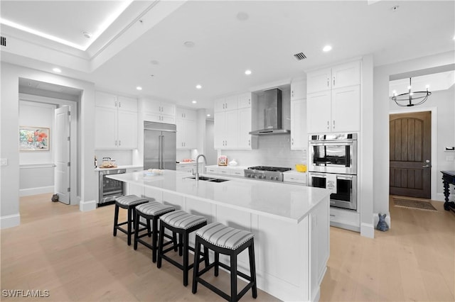 16304 Corsica Way Unit 101, Naples, FL 34110 - kitchen with appliances with stainless steel finishes, a sink, wall chimney exhaust hood, wine cooler, and a kitchen breakfast bar