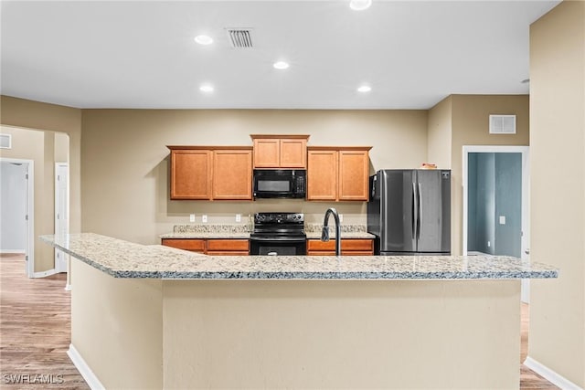 2211 SW 12th Ln, Cape Coral, FL 33991 - kitchen with black appliances, light wood-type flooring, an island with sink, light stone countertops, and recessed lighting
