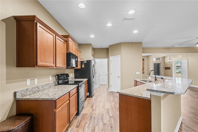 2211 SW 12th Ln, Cape Coral, FL 33991 - kitchen with black appliances, light wood-type flooring, an island with sink, brown cabinets, and light stone counters
