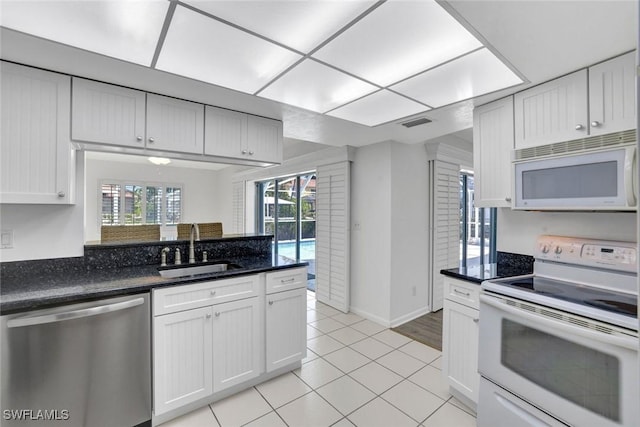 53 Madagascar Ct, Marco Island, FL 34145 - kitchen with white appliances, white cabinets, light tile patterned floors, dark stone counters, and a peninsula