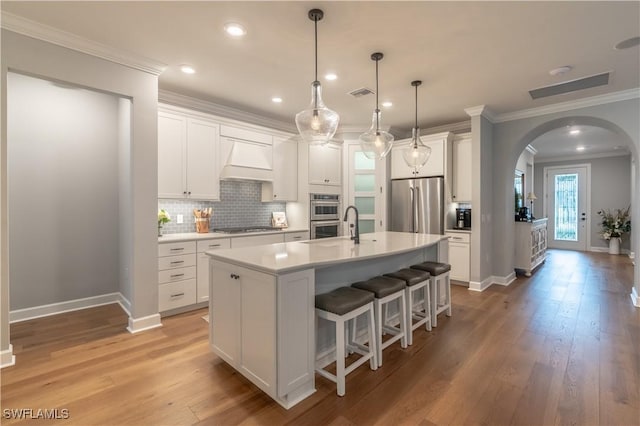6848 Winding Cypress Dr, Naples, FL 34114 - kitchen featuring stainless steel appliances, arched walkways, premium range hood, baseboards, and ornamental molding