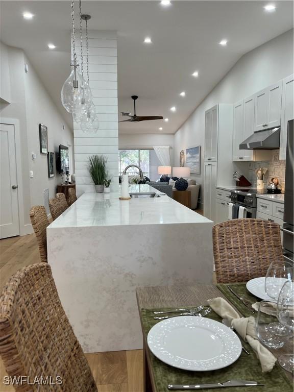 7087 Barrington Cir Unit 201, Naples, FL 34108 - kitchen featuring under cabinet range hood, vaulted ceiling, stainless steel range with electric stovetop, ceiling fan, and decorative backsplash