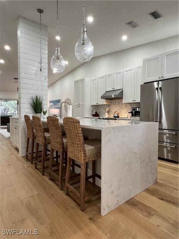 7087 Barrington Cir Unit 201, Naples, FL 34108 - kitchen with stainless steel refrigerator, light wood-style flooring, under cabinet range hood, decorative backsplash, and a breakfast bar