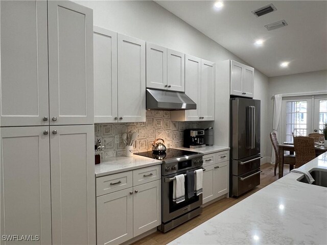 7087 Barrington Cir Unit 201, Naples, FL 34108 - kitchen featuring appliances with stainless steel finishes, under cabinet range hood, vaulted ceiling, backsplash, and light wood-type flooring