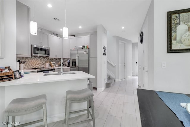 7501 Carnegie Way, Naples, FL 34119 - kitchen featuring stainless steel appliances, a breakfast bar, tasteful backsplash, hanging light fixtures, and light countertops
