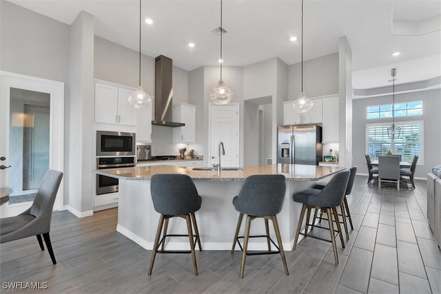 15889 Cranes Marsh Ct, Punta Gorda, FL 33982 - kitchen featuring appliances with stainless steel finishes, wall chimney exhaust hood, a sink, light wood-style flooring, and a large island with sink