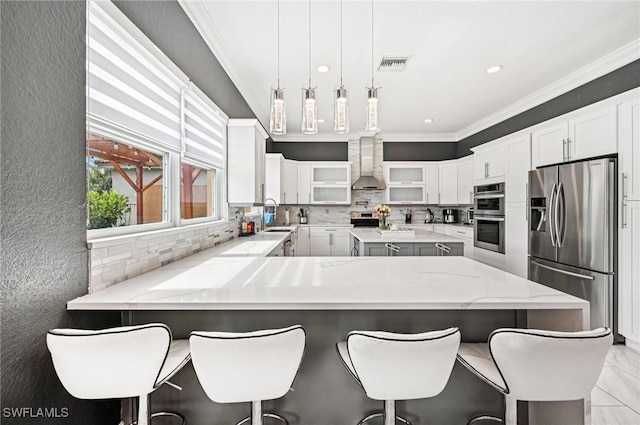 7082 Aliso Ave, West Palm Beach, FL 33413 - kitchen with stainless steel appliances, tasteful backsplash, ornamental molding, wall chimney range hood, and a peninsula