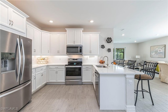 1050 Enbrook Loop, Naples, FL 34114 - kitchen with stainless steel appliances, a sink, a peninsula, a kitchen bar, and light wood-style flooring