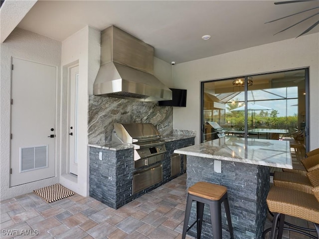 19449 The Place Blvd, Estero, FL 33928 - kitchen with wall chimney exhaust hood, stone tile floors, a kitchen breakfast bar, and light stone countertops