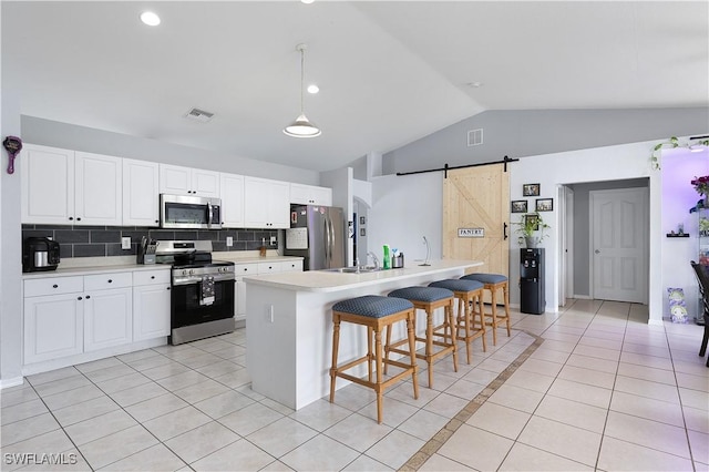 866 Carbon St E, Lehigh Acres, FL 33974 - kitchen featuring appliances with stainless steel finishes, a barn door, vaulted ceiling, light tile patterned flooring, and light countertops