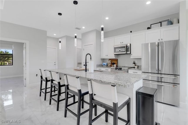 4119 43rd Ave NE, Naples, FL 34120 - kitchen with stainless steel appliances, light marble finish flooring, white cabinets, a center island with sink, and recessed lighting