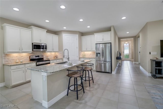 14594 Tropical Dr, Naples, FL 34114 - kitchen with stainless steel appliances, a sink, decorative backsplash, a center island with sink, and white cabinetry