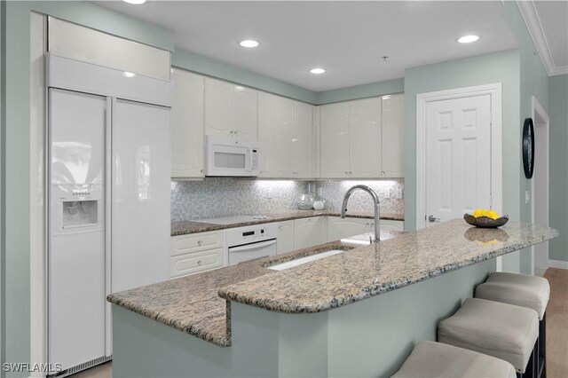 740 N Collier Blvd Unit 206, Marco Island, FL 34145 - kitchen with white appliances, a kitchen bar, white cabinets, a sink, and backsplash