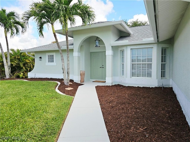 1221 SW 10th Ter, Cape Coral, FL 33991 - view of exterior entry featuring stucco siding, a lawn, and roof with shingles