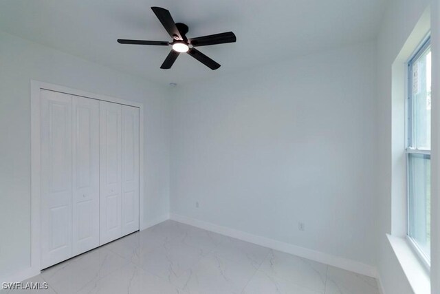 2501 26th St W, Lehigh Acres, FL 33971 - unfurnished bedroom featuring light marble finish floors, multiple windows, a closet, and a ceiling fan
