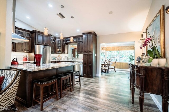 1440 14th Ave NE, Naples, FL 34120 - kitchen featuring stainless steel appliances, dark brown cabinets, wood finished floors, light stone countertops, and a breakfast bar area