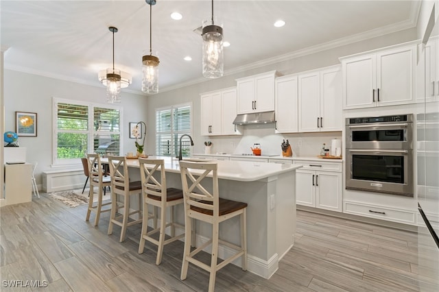 kitchen featuring light countertops, stainless steel double oven, an island with sink, light wood-style flooring, and recessed lighting