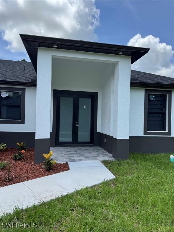3003 18th St W, Lehigh Acres, FL 33976 - entrance to property featuring stucco siding, a shingled roof, french doors, and a yard