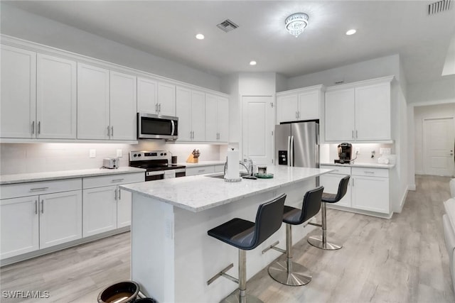 3320 41st Ave NE, Naples, FL 34120 - kitchen featuring appliances with stainless steel finishes, a kitchen bar, white cabinetry, light wood-type flooring, and recessed lighting