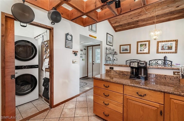 7786 Breakwater Ct, Bokeelia, FL 33922 - kitchen featuring stacked washer / dryer, light tile patterned floors, brown cabinetry, dark stone countertops, and wood ceiling