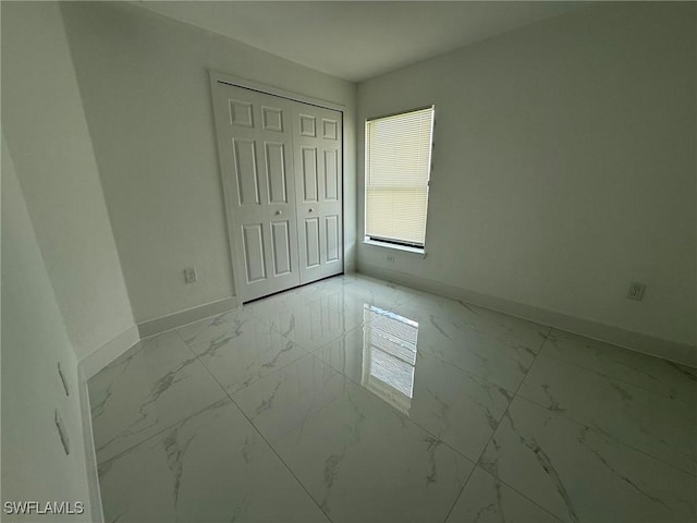 3508 17th St SW, Lehigh Acres, FL 33976 - unfurnished bedroom featuring baseboards, light marble finish flooring, and a closet