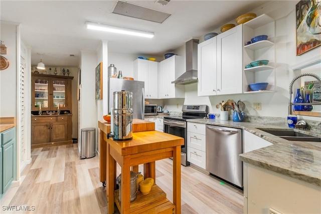 5228 Stringfellow Rd, Saint James City, FL 33956 - kitchen featuring stainless steel appliances, wall chimney range hood, light wood-style floors, and white cabinets