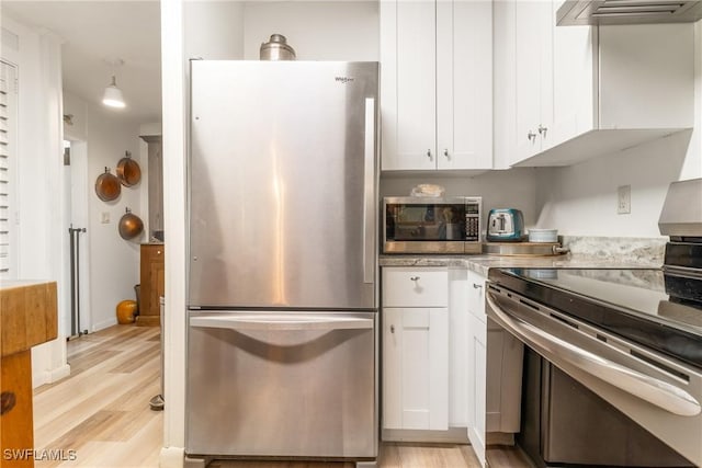5228 Stringfellow Rd, Saint James City, FL 33956 - kitchen featuring stainless steel appliances, light wood-style flooring, white cabinets, exhaust hood, and light countertops