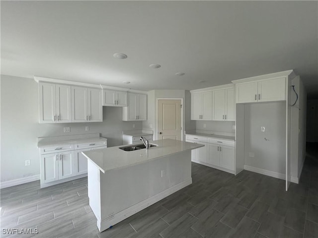 658 Ivanhoe Ave S, Lehigh Acres, FL 33974 - kitchen with a sink, wood tiled floors, baseboards, white cabinetry, and a center island with sink