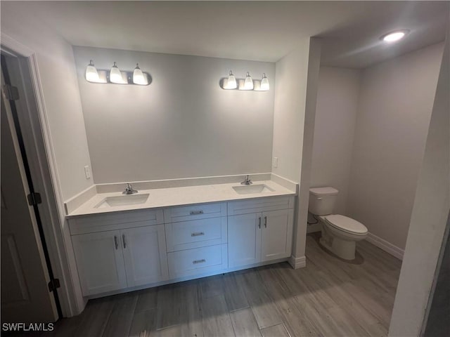 658 Ivanhoe Ave S, Lehigh Acres, FL 33974 - full bathroom featuring wood finished floors, toilet, double vanity, and baseboards