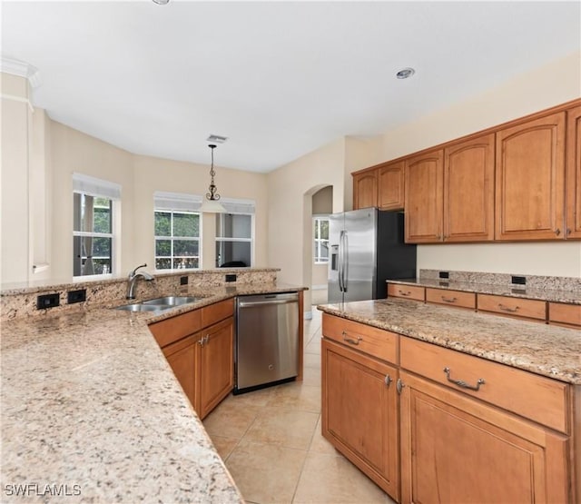 17091 Laurelin Ct, North Fort Myers, FL 33917 - kitchen featuring stainless steel appliances, arched walkways, light stone counters, brown cabinetry, and decorative light fixtures