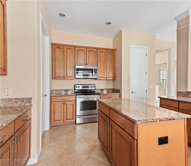 17091 Laurelin Ct, North Fort Myers, FL 33917 - kitchen with stainless steel appliances, a center island, light stone countertops, light tile patterned floors, and brown cabinets