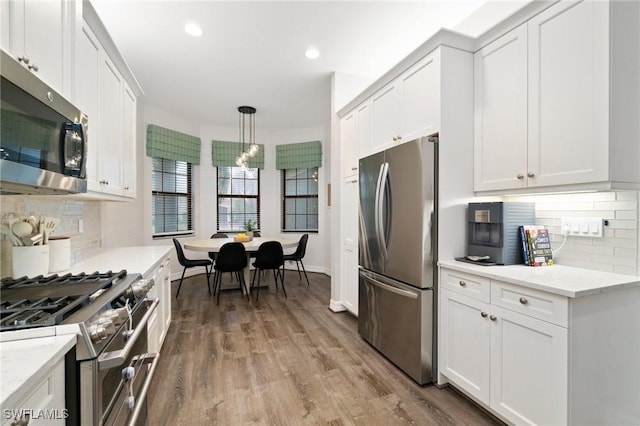 4119 Zelkova Ct, Naples, FL 34119 - kitchen with stainless steel appliances, white cabinetry, wood finished floors, backsplash, and decorative light fixtures