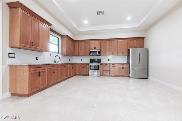 10295 Carolina St, Bonita Springs, FL 34135 - kitchen with stainless steel appliances, a raised ceiling, decorative backsplash, and brown cabinetry