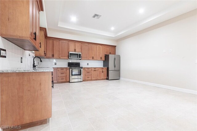 10295 Carolina St, Bonita Springs, FL 34135 - kitchen with stainless steel appliances, a tray ceiling, light stone counters, brown cabinets, and recessed lighting