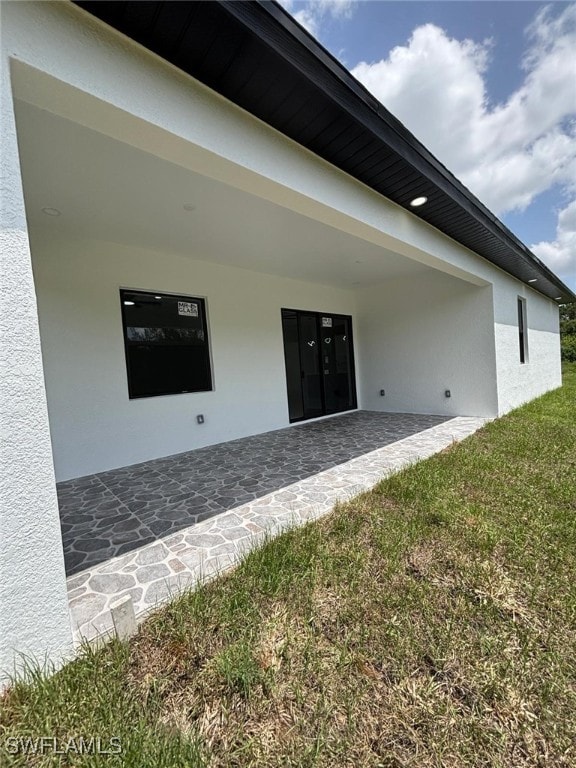 2909 Dora Ave N, Lehigh Acres, FL 33971 - view of exterior entry featuring stucco siding, a lawn, and a patio area