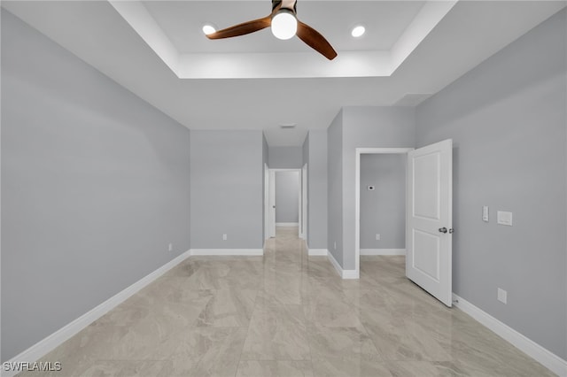 908 Barcia St E, Lehigh Acres, FL 33974 - empty room featuring a ceiling fan, a tray ceiling, light marble finish flooring, and baseboards