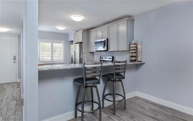 3451 County Barn Rd Unit G103, Naples, FL 34112 - kitchen with stainless steel appliances, light wood finished floors, a kitchen breakfast bar, a peninsula, and light stone countertops