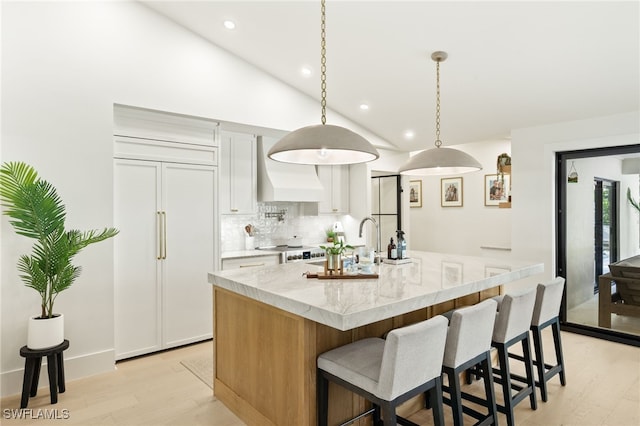 7658 Ponte Verde Way, Naples, FL 34109 - kitchen with paneled built in fridge, custom range hood, light wood-style flooring, decorative backsplash, and a center island with sink