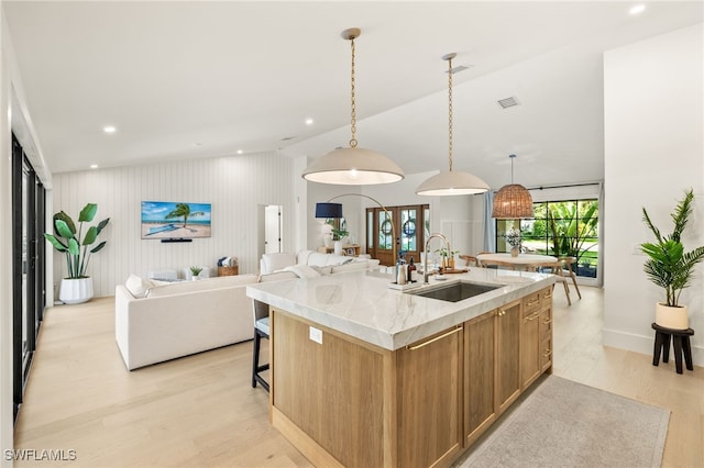 7658 Ponte Verde Way, Naples, FL 34109 - kitchen with light wood-style flooring, open floor plan, a kitchen island with sink, brown cabinetry, and pendant lighting
