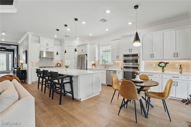 17467 Caravita Ln, Fort Myers, FL 33913 - kitchen with stainless steel appliances, under cabinet range hood, ornamental molding, tasteful backsplash, and a breakfast bar area