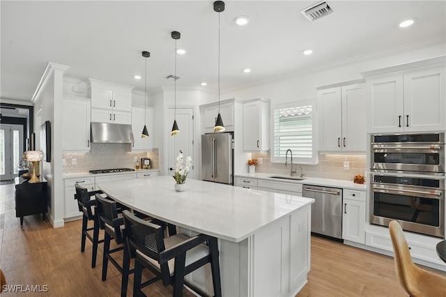 17467 Caravita Ln, Fort Myers, FL 33913 - kitchen featuring appliances with stainless steel finishes, under cabinet range hood, a center island, backsplash, and ornamental molding