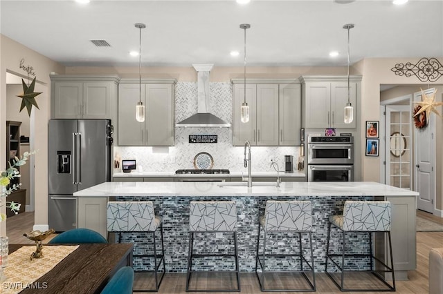 42274 Waterfront Way, Punta Gorda, FL 33982 - kitchen featuring appliances with stainless steel finishes, wall chimney exhaust hood, an island with sink, backsplash, and light wood-style floors