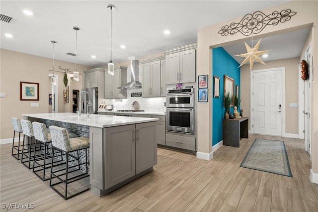 42274 Waterfront Way, Punta Gorda, FL 33982 - kitchen featuring wall chimney exhaust hood, gray cabinetry, appliances with stainless steel finishes, a kitchen bar, and recessed lighting