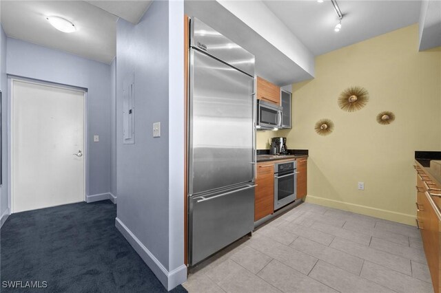 3000 Oasis Grand Blvd Unit 906, Fort Myers, FL 33916 - kitchen featuring appliances with stainless steel finishes, brown cabinets, track lighting, and dark countertops